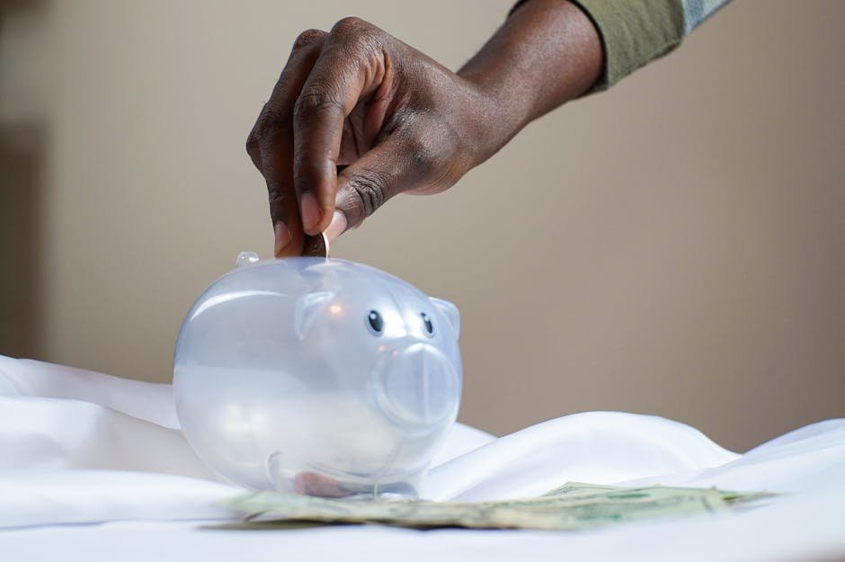 Hand placing coins into a transparent piggy bank